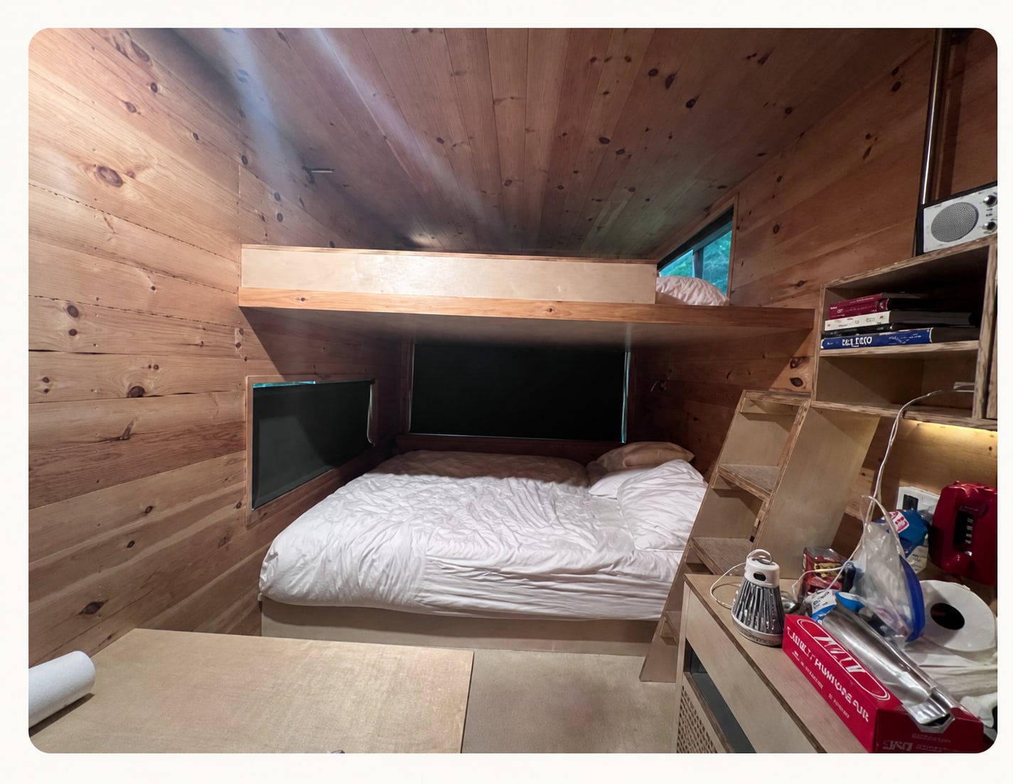 Compact wood-paneled Postcard Cabin interior with queen bed, loft, ladder, shelves, and cabin amenities